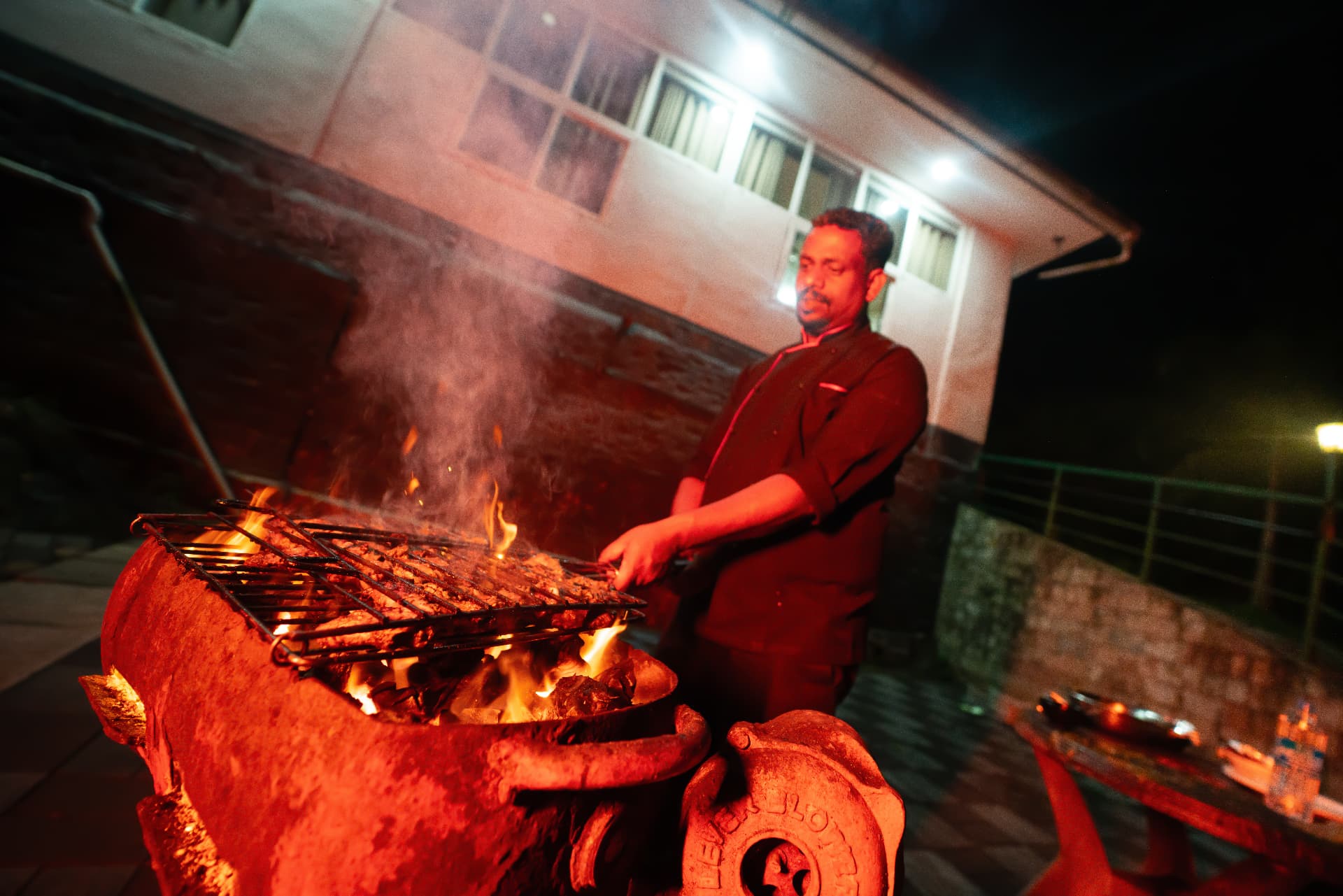 Chef grilling kebabs over open coals at night outside the restaurant at Grand Valley Resort, Munnar